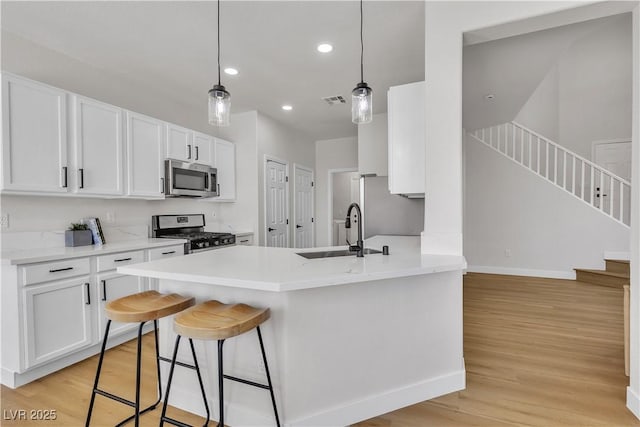 kitchen featuring stainless steel appliances, a sink, light wood finished floors, white cabinetry, and baseboards
