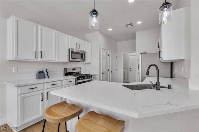 kitchen featuring stainless steel appliances, a sink, white cabinets, a peninsula, and light stone countertops
