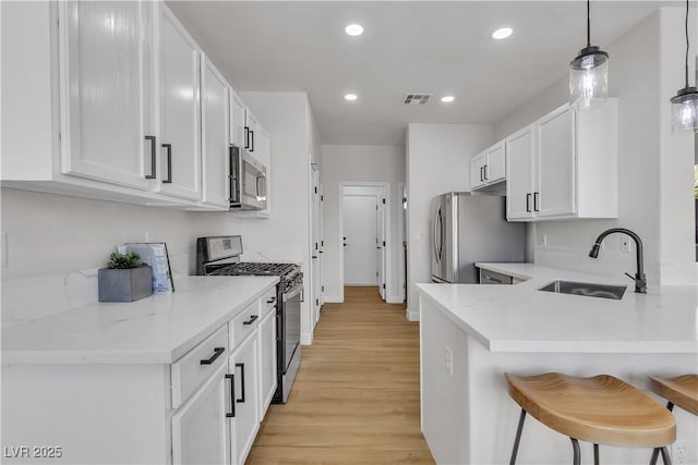 kitchen with stainless steel appliances, a sink, a breakfast bar area, light wood finished floors, and white cabinetry