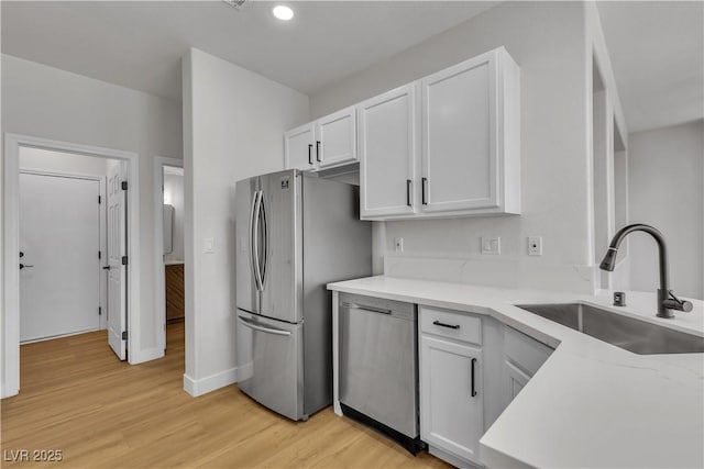 kitchen with a sink, stainless steel appliances, white cabinetry, light wood finished floors, and baseboards