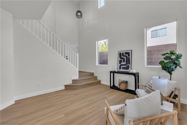 living room with stairway, wood finished floors, baseboards, and a towering ceiling