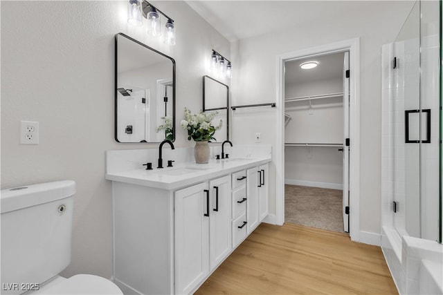bathroom featuring a shower with shower door, toilet, wood finished floors, a spacious closet, and double vanity