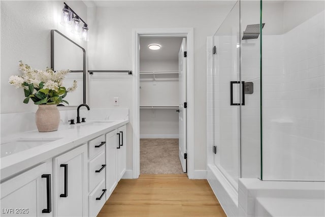 bathroom featuring a shower stall, a walk in closet, wood finished floors, and double vanity