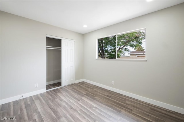 unfurnished bedroom with baseboards, wood finished floors, a closet, and recessed lighting