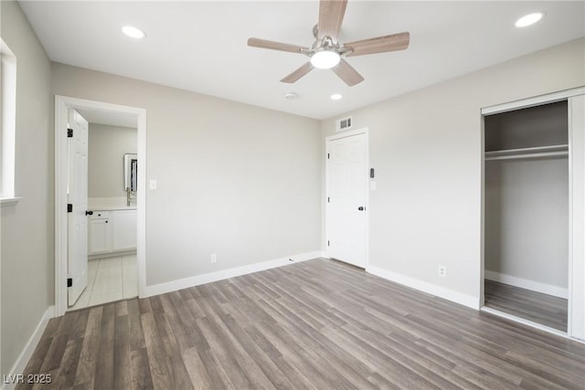unfurnished bedroom with wood finished floors, a closet, recessed lighting, ensuite bath, and baseboards