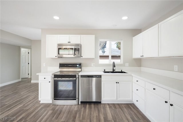 kitchen with appliances with stainless steel finishes, a sink, wood finished floors, white cabinetry, and light countertops