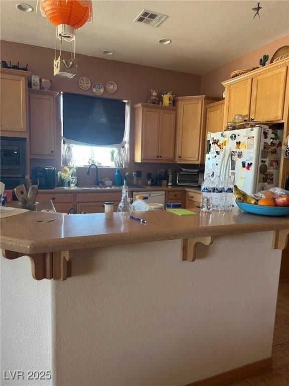 3551 Sagebrush Ave, Pahrump, NV 89048 - kitchen with a breakfast bar area, white refrigerator with ice dispenser, stainless steel dishwasher, a sink, and built in microwave