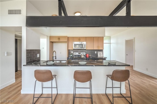 kitchen featuring appliances with stainless steel finishes, a sink, a peninsula, dark countertops, and beam ceiling