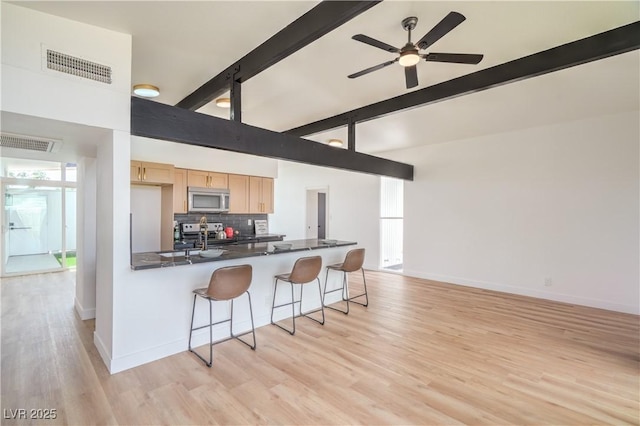 kitchen featuring appliances with stainless steel finishes, light brown cabinets, a breakfast bar area, beam ceiling, and dark countertops