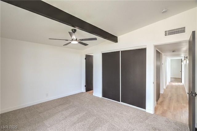 unfurnished bedroom featuring beamed ceiling, baseboards, a closet, light colored carpet, and ceiling fan