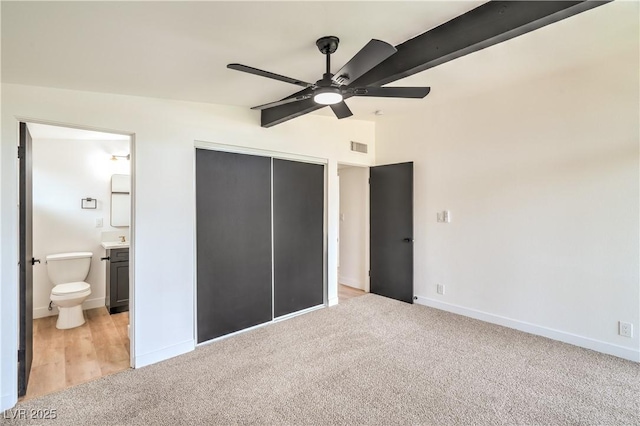 unfurnished bedroom with light carpet, a closet, baseboards, lofted ceiling, and ensuite bathroom