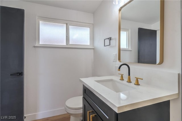half bath featuring vanity, toilet, wood finished floors, and baseboards