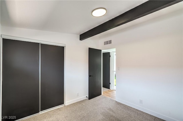 unfurnished bedroom with beam ceiling, light colored carpet, baseboards, and a closet