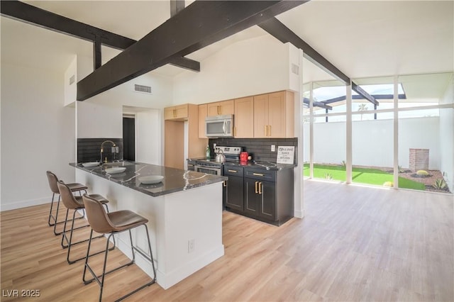 kitchen with appliances with stainless steel finishes, dark countertops, a breakfast bar area, tasteful backsplash, and a sink