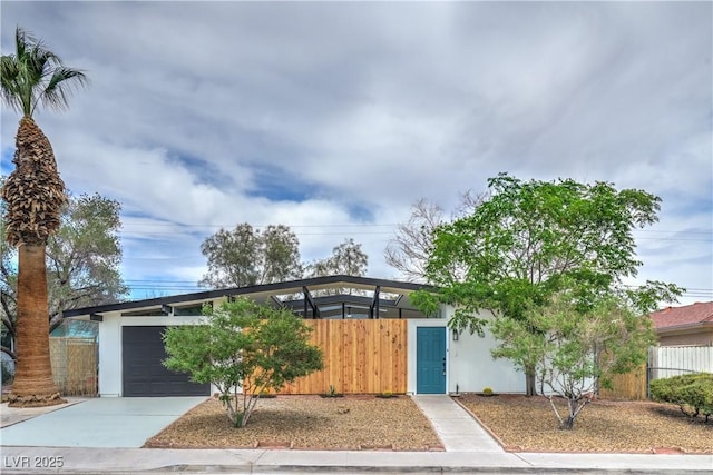 mid-century home with a fenced front yard, driveway, and a garage