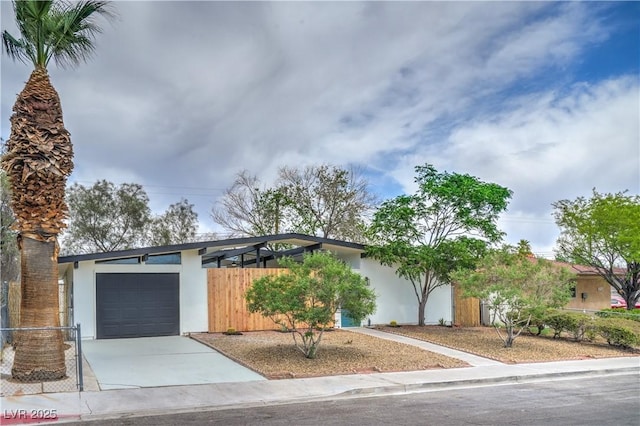 view of front of home with stucco siding, a garage, concrete driveway, and fence