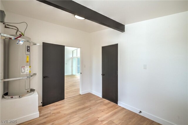 unfurnished room with baseboards, light wood-style flooring, beamed ceiling, and water heater