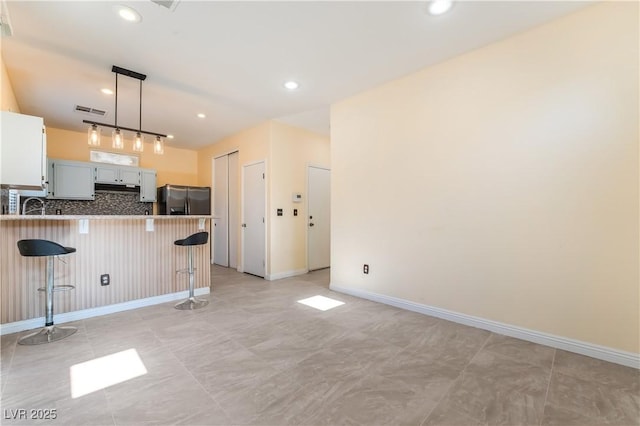 9753 Villa Lorena Ave, Las Vegas, NV 89147 - kitchen featuring stainless steel fridge, a kitchen breakfast bar, a peninsula, tasteful backsplash, and decorative light fixtures