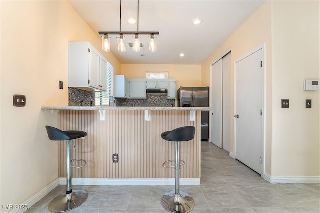 9753 Villa Lorena Ave, Las Vegas, NV 89147 - kitchen featuring stainless steel refrigerator with ice dispenser, a peninsula, a breakfast bar, baseboards, and tasteful backsplash