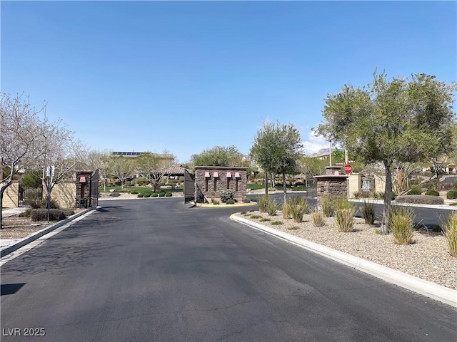 view of asphalt street with curbs, a gated entry, and traffic signs
