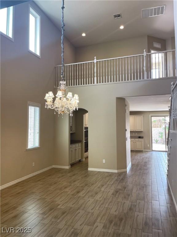 unfurnished living room featuring a high ceiling, arched walkways, wood finished floors, healthy amount of natural light, and baseboards