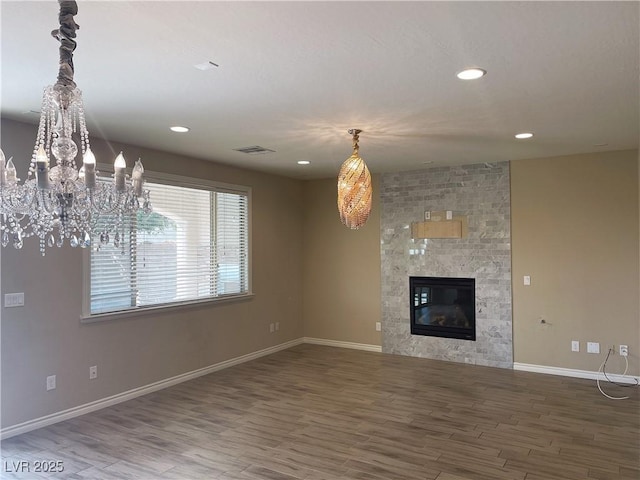 unfurnished living room with wood finished floors, baseboards, recessed lighting, a large fireplace, and a chandelier
