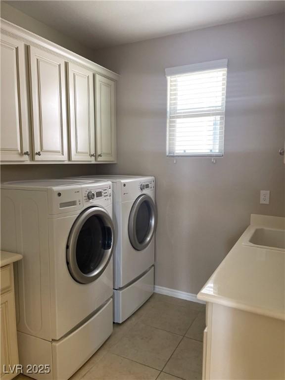 washroom featuring washing machine and dryer, cabinet space, light tile patterned floors, and baseboards