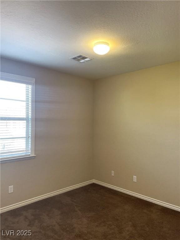 spare room featuring dark carpet, baseboards, and a textured ceiling
