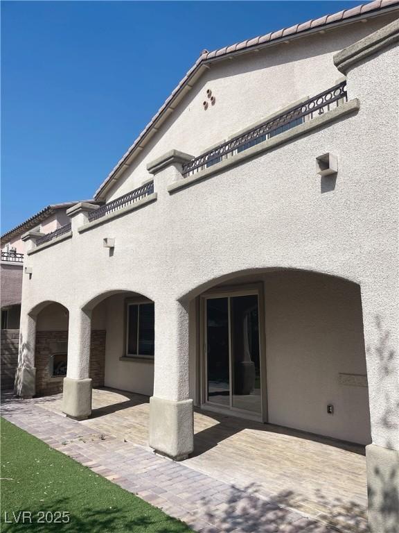 rear view of property featuring a patio area, stucco siding, and a tiled roof