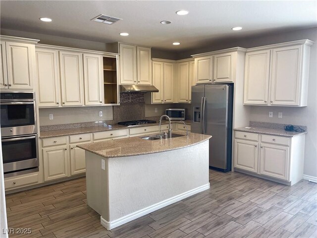 kitchen with a sink, appliances with stainless steel finishes, light wood-style floors, light stone counters, and recessed lighting