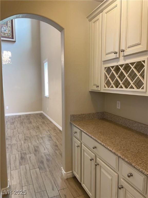 kitchen featuring arched walkways, baseboards, light stone counters, light wood finished floors, and cream cabinetry
