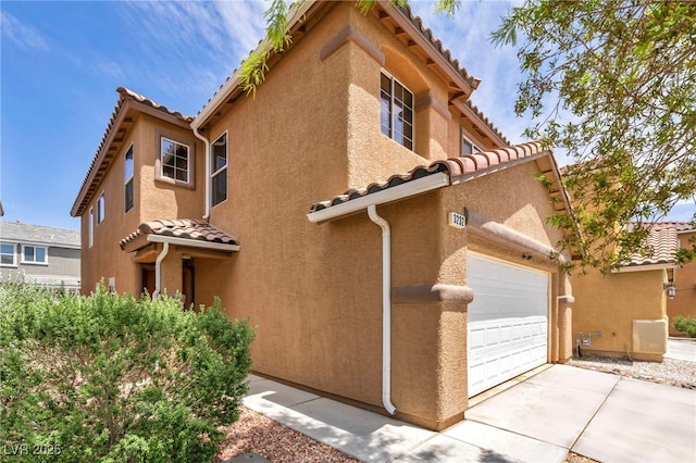 view of side of property with a tile roof, a garage, concrete driveway, and stucco siding