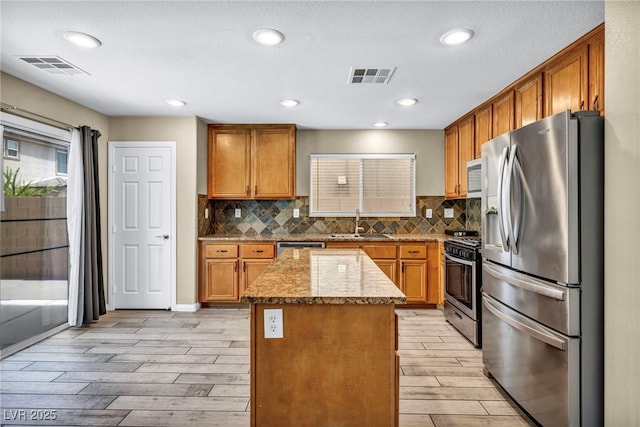 kitchen with stainless steel appliances, a sink, light wood-style flooring, a kitchen island, and brown cabinetry