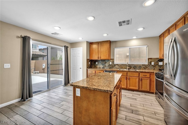 kitchen featuring appliances with stainless steel finishes, wood finish floors, brown cabinetry, backsplash, and recessed lighting