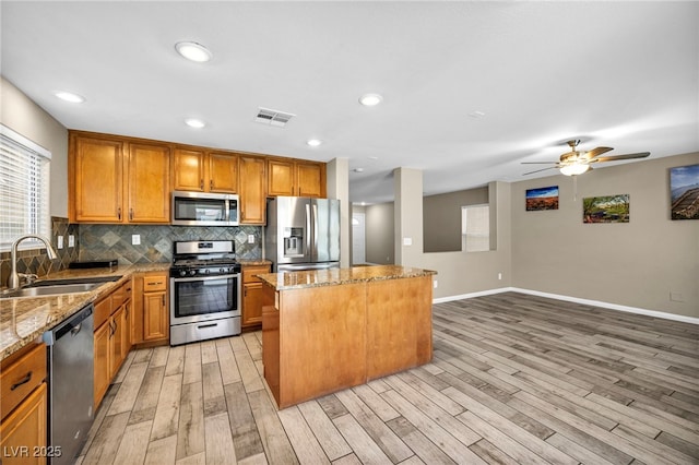 kitchen featuring stainless steel appliances, a sink, light wood-style floors, a kitchen island, and tasteful backsplash