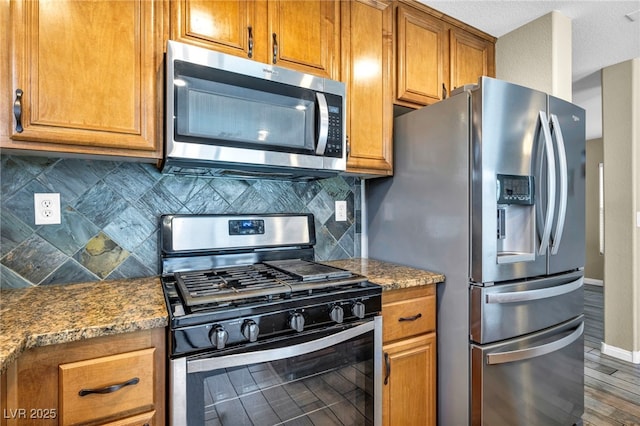 kitchen with appliances with stainless steel finishes, baseboards, brown cabinets, backsplash, and wood finished floors