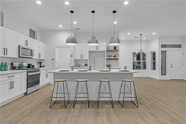 10801 Clarion Ln, Las Vegas, NV 89134 - kitchen featuring appliances with stainless steel finishes, an island with sink, white cabinets, light wood-type flooring, and light countertops
