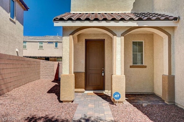 property entrance with stucco siding, fence, and a tiled roof