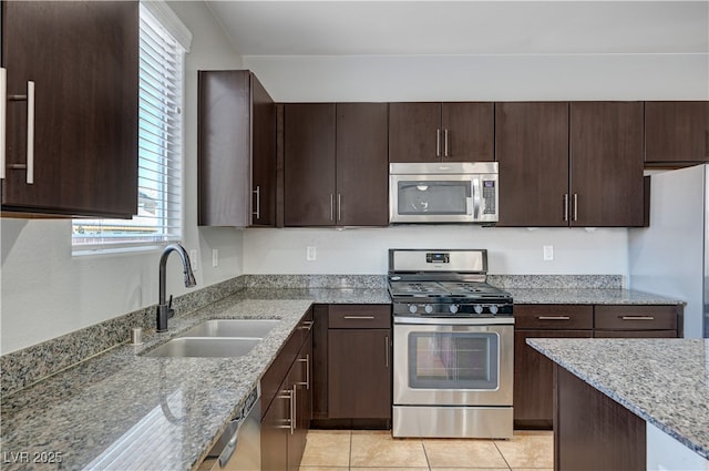 kitchen featuring stainless steel appliances, a sink, dark brown cabinets, and light stone counters