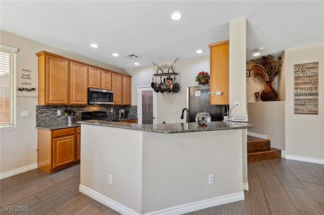 kitchen featuring appliances with stainless steel finishes, dark stone countertops, wood tiled floors, baseboards, and recessed lighting