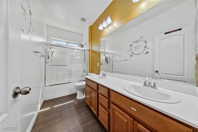 bathroom with double vanity, combined bath / shower with glass door, and toilet