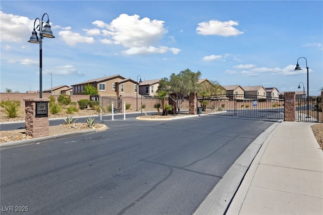 view of asphalt road with a residential view, a gate, street lights, and sidewalks