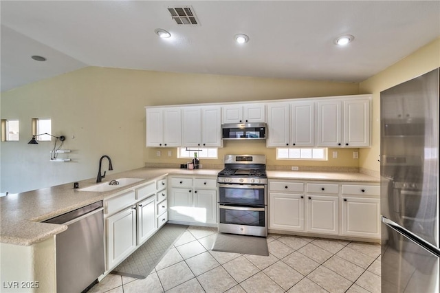 kitchen with appliances with stainless steel finishes, a sink, vaulted ceiling, a peninsula, and white cabinetry