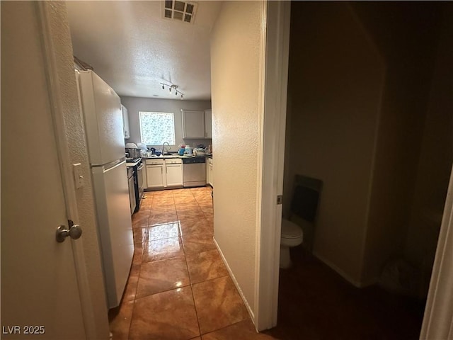 corridor featuring a textured wall, a textured ceiling, light tile patterned flooring, and a sink