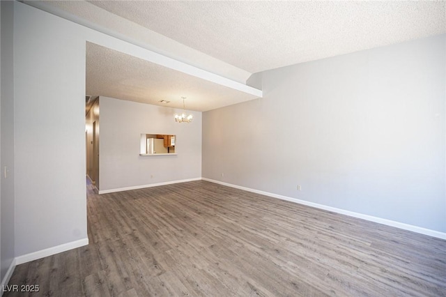 empty room featuring a chandelier, wood finished floors, baseboards, and a textured ceiling