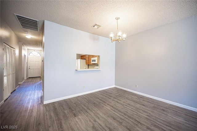unfurnished room featuring a chandelier, dark wood-style floors, a textured ceiling, and baseboards
