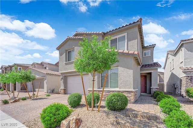 mediterranean / spanish home featuring an attached garage, a tile roof, stone siding, and a gate