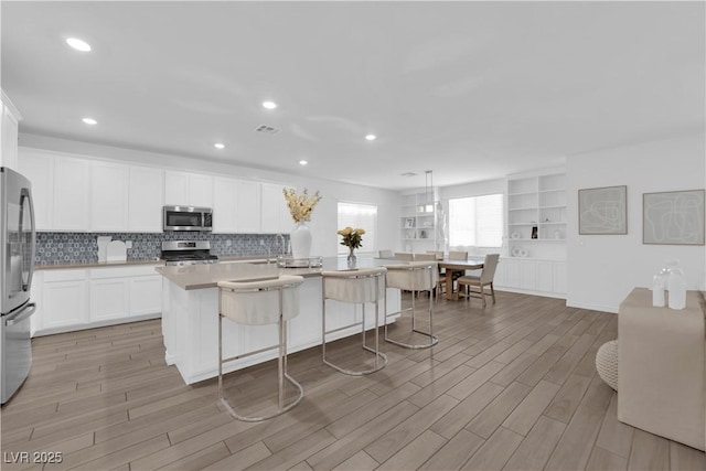 kitchen with stainless steel appliances, light wood-style floors, decorative backsplash, a breakfast bar, and recessed lighting