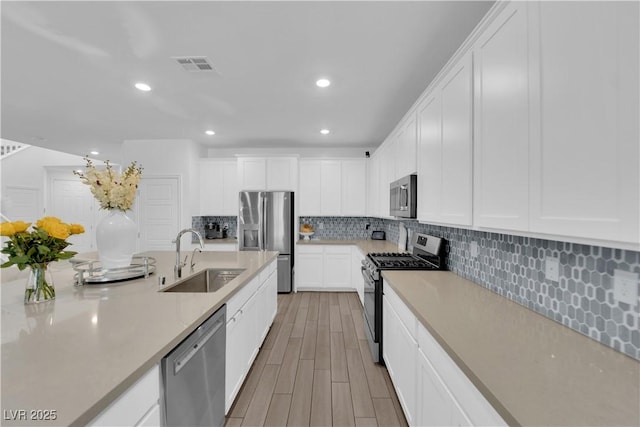 kitchen with appliances with stainless steel finishes, a sink, backsplash, light countertops, and recessed lighting