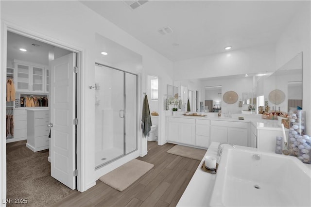 full bathroom with a stall shower, vanity, a walk in closet, a bathtub, and wood finished floors